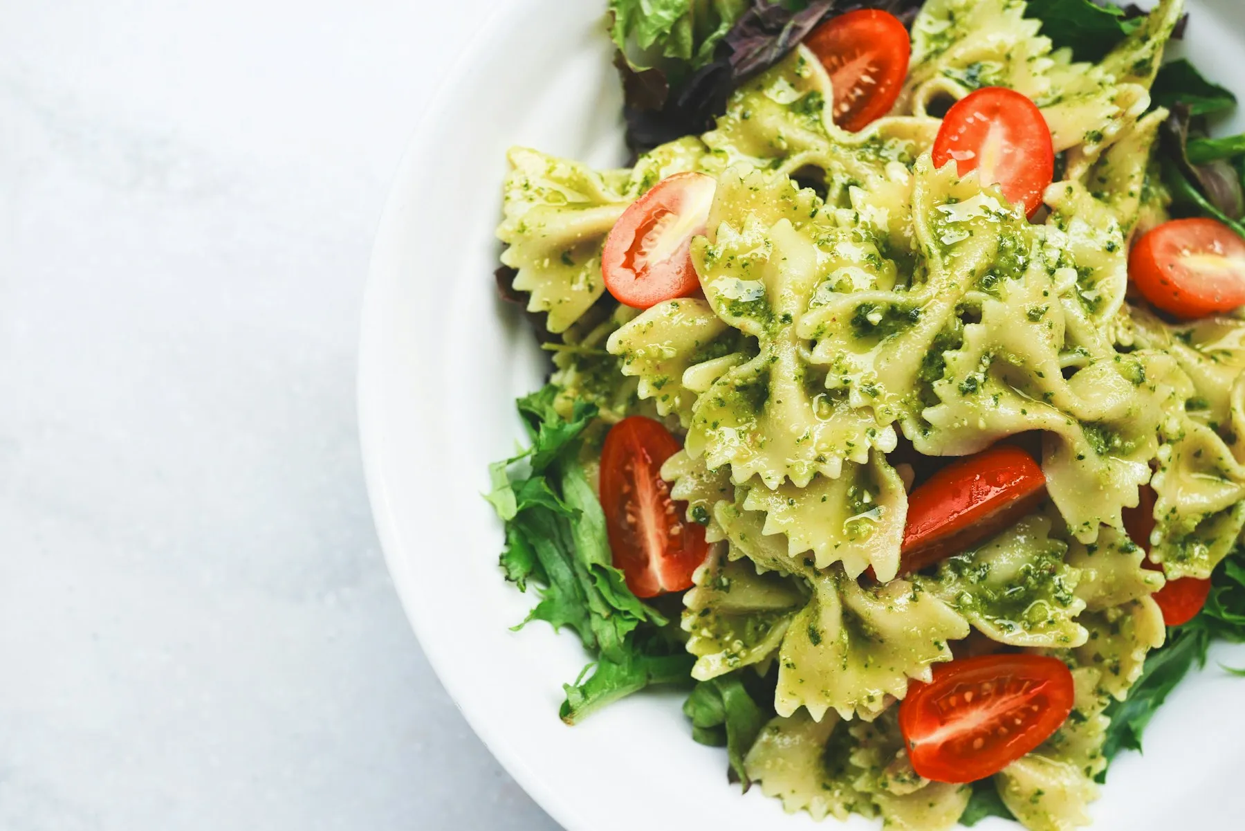 Pasta mit Pesto, Kirschtomaten und frischen Blättern auf hellem Teller